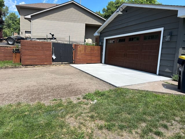 Newly poured concrete driveway apron in front of a detached garage with dark wood-style doors.