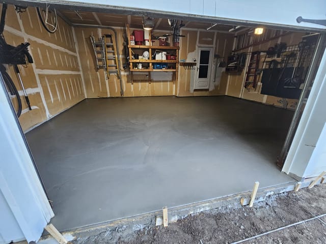 Freshly poured concrete garage floor inside an open residential garage, with a smooth gray finish.