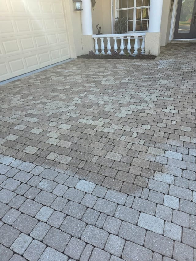 Paver driveway in front of a home, with mixed gray and tan stones leading to a garage and covered entryway.
