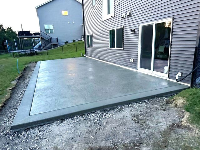 Newly poured concrete patio with a decorative stamped finish extending from the back of a house.