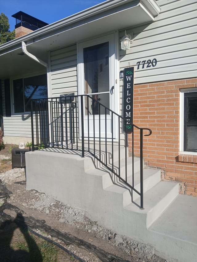 Newly constructed concrete front steps and landing with black metal railings leading to a home's front entrance.