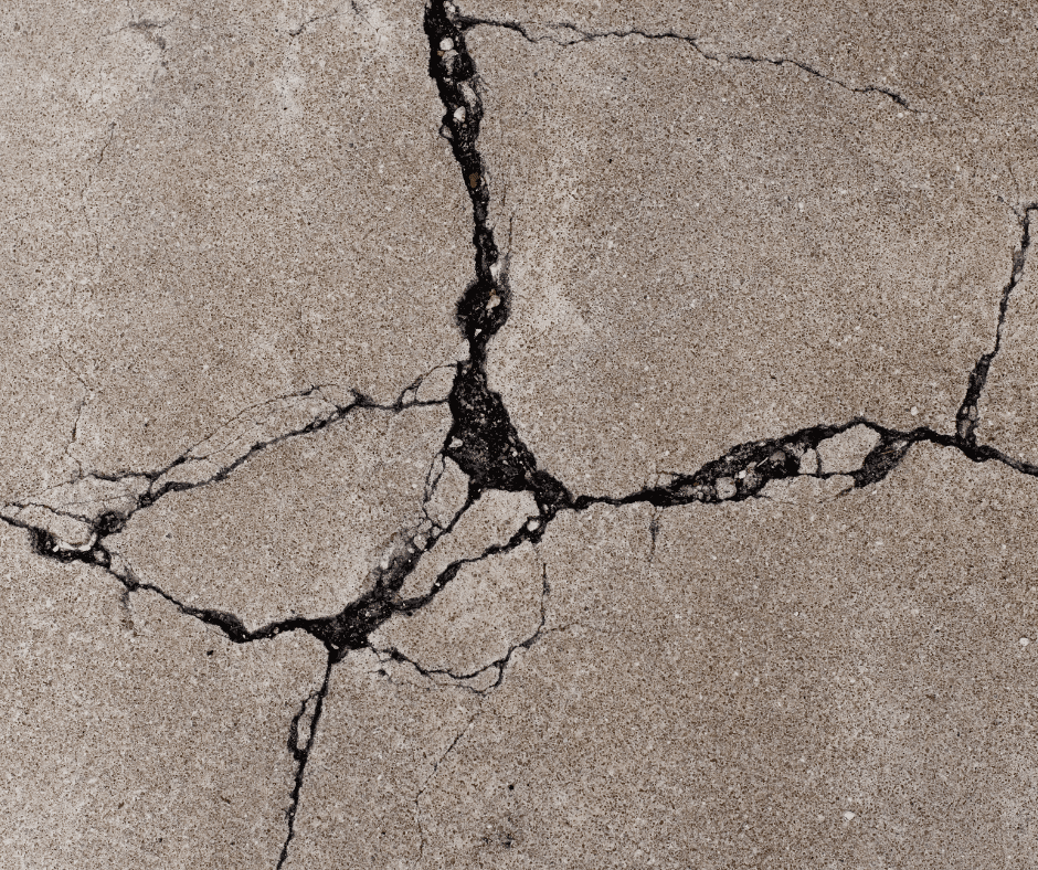 Close-up of cracked concrete before concrete driveway replacement, with wide dark fractures across the surface.