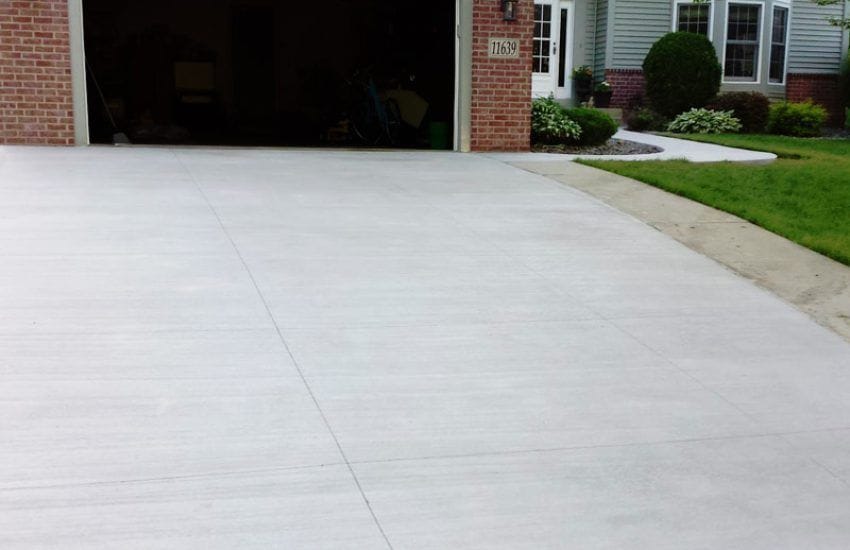 Bright new concrete driveway with a broom finish and clean control joints in front of a garage.