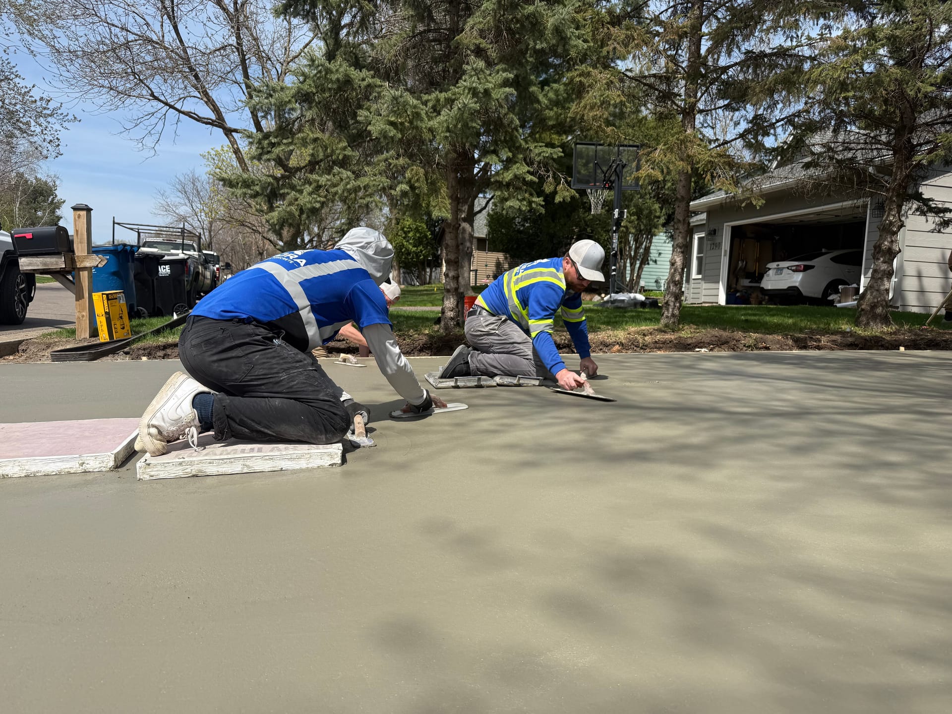 Concrete driveway contractor crew kneeling on boards to hand-finish a freshly poured residential driveway.