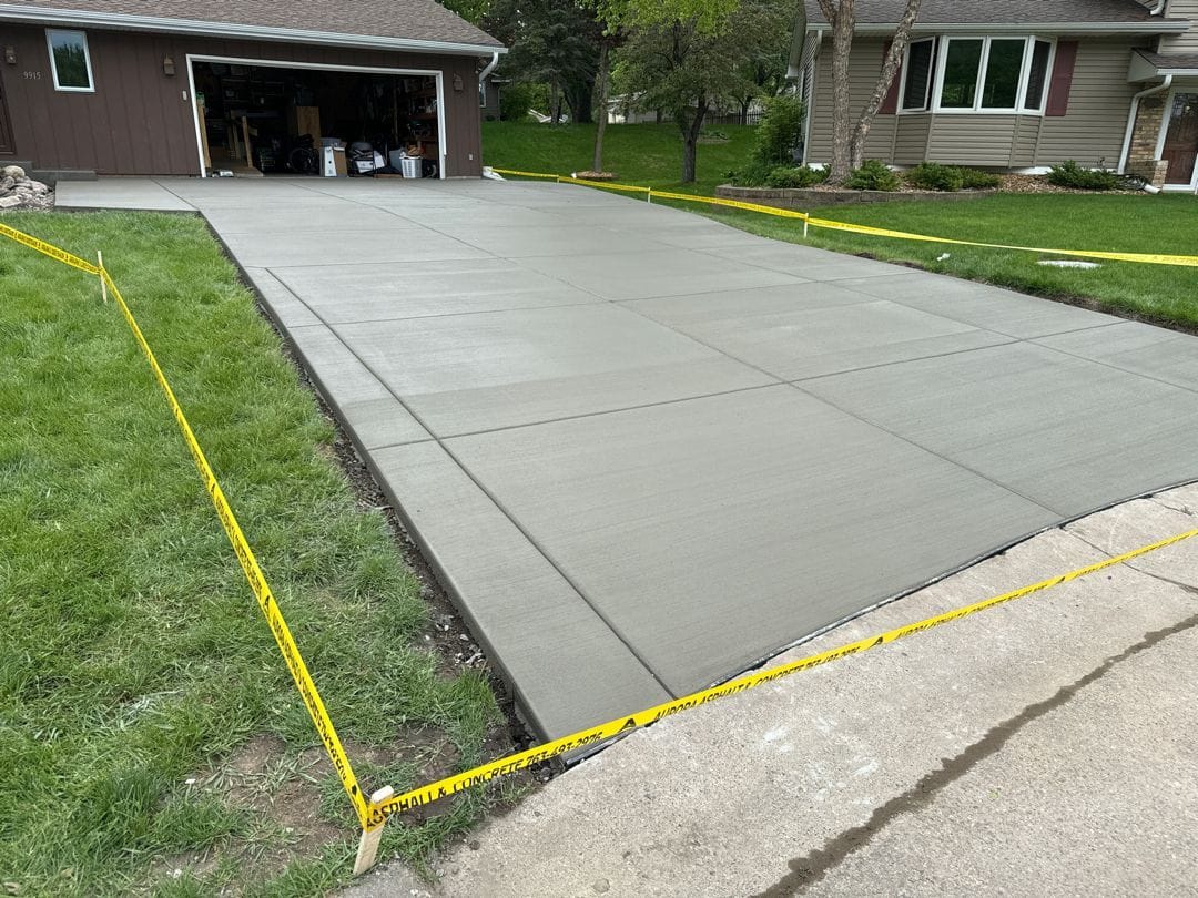 Concrete driveway installation in progress, with fresh concrete, forms, and caution tape along the edges.