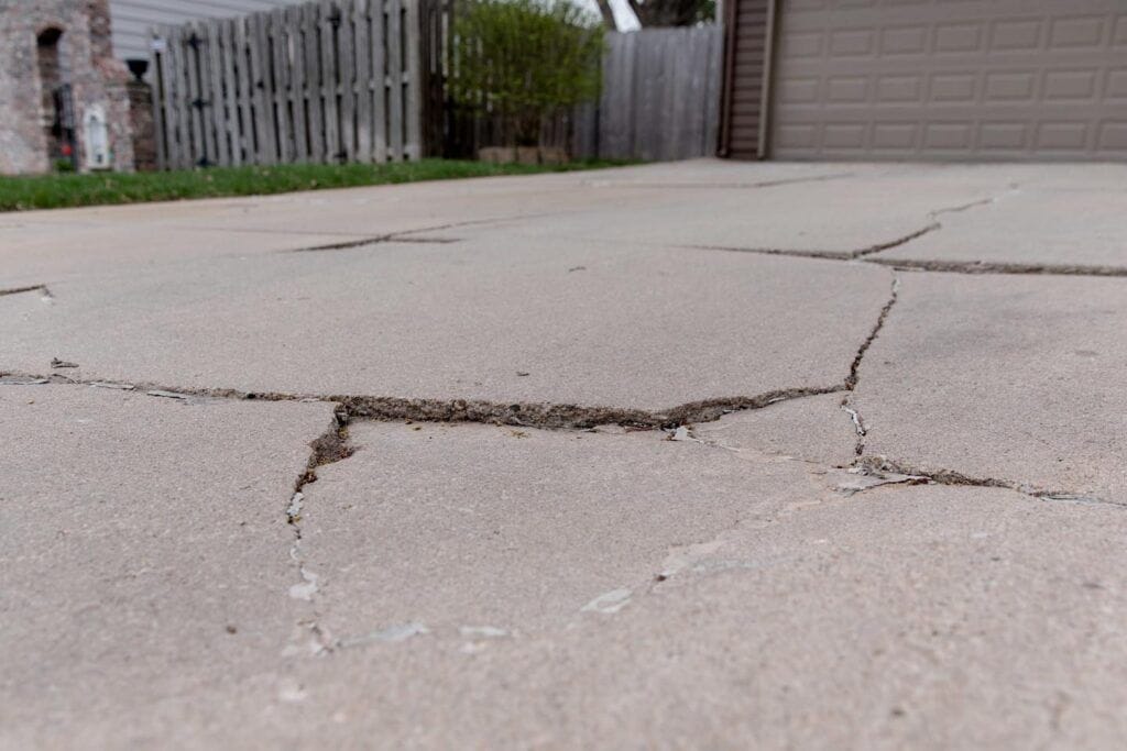 Cracked, settling concrete in front of a garage that needs concrete driveway repair.