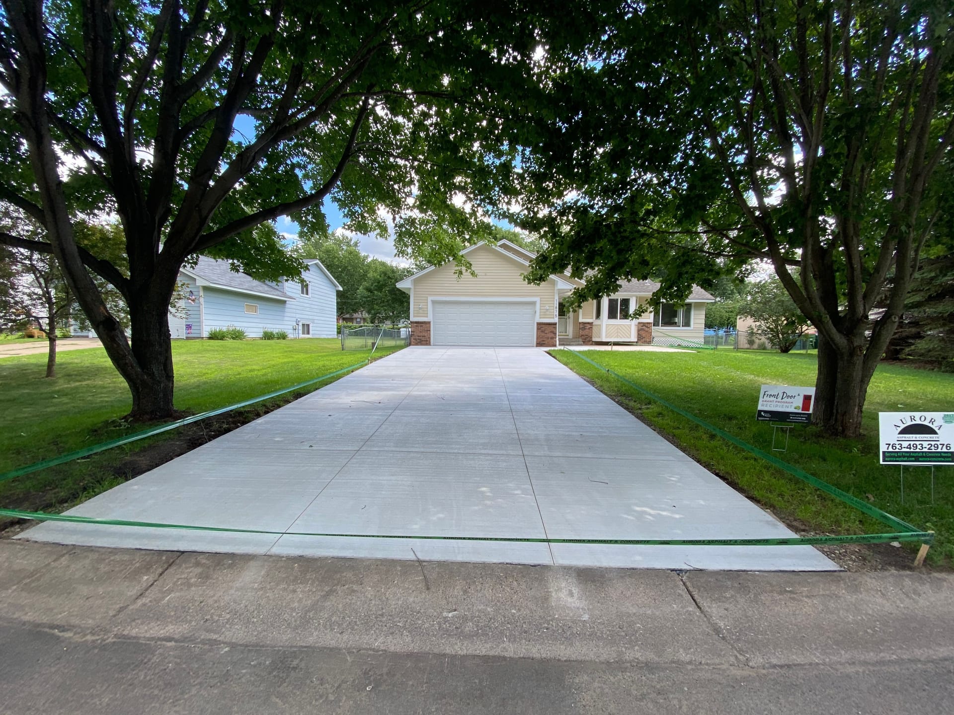 Smooth, crack-free concrete driveway lined by trees, the result of cracked concrete driveway repair.