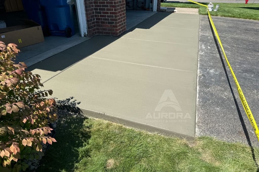 Fresh concrete strip extending a driveway beside a garage, poured by a driveway extension contractor.