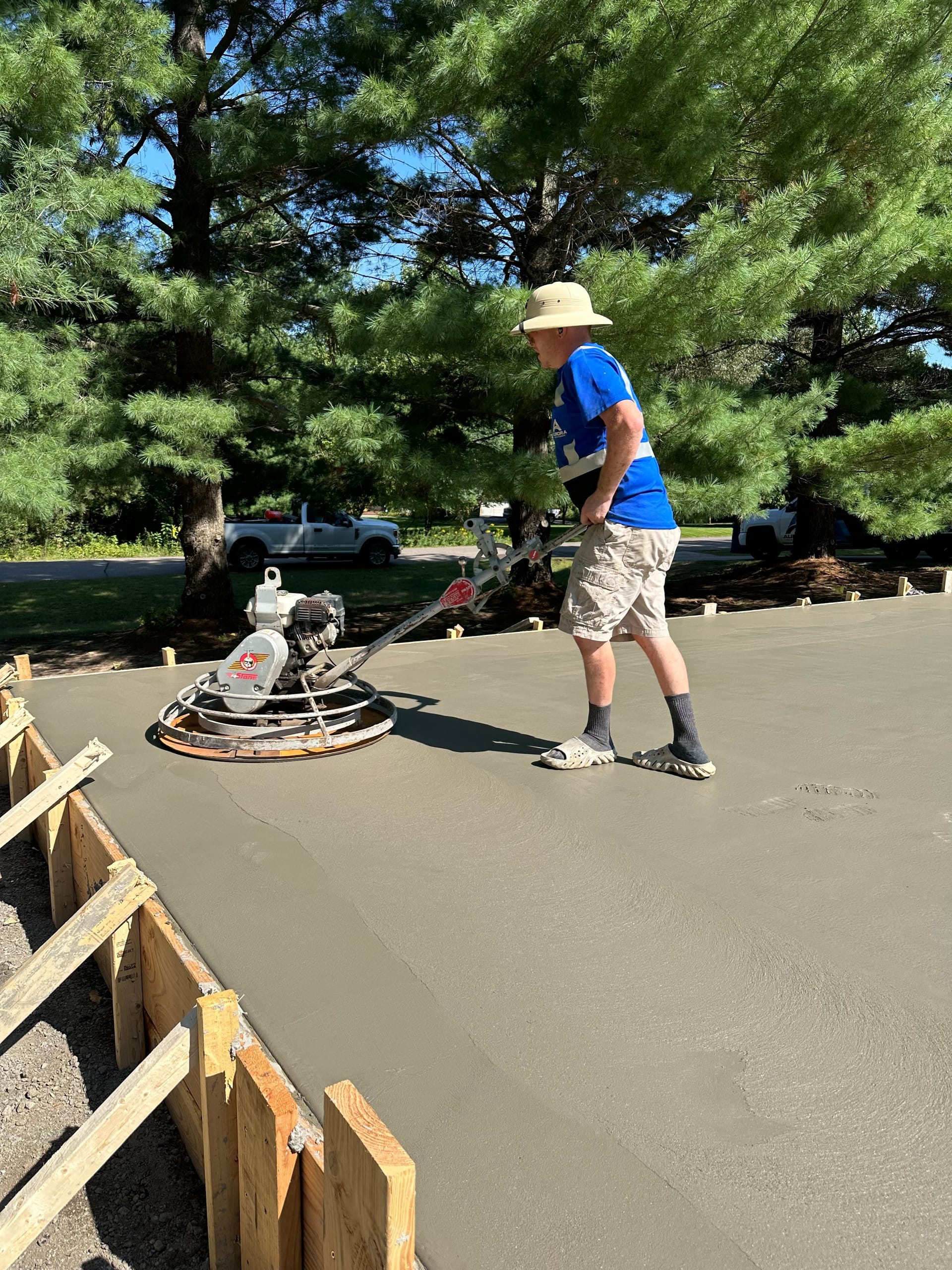 Crew member power-troweling a new concrete driveway inside wooden forms.